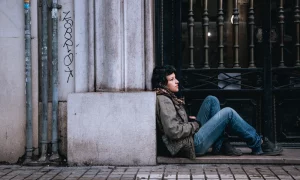 Jeune femme assise par terre dans la rue contre un mur
